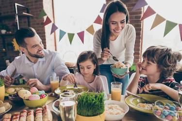 Eine Familie sitzt zum Osterbrunch zusammen. Den Tisch zieren österliche Leckereien.