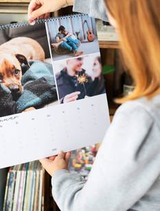 Wandkalender in unterschiedlichen Design hängen über einer Kommode und einem Sessel an der Wand.