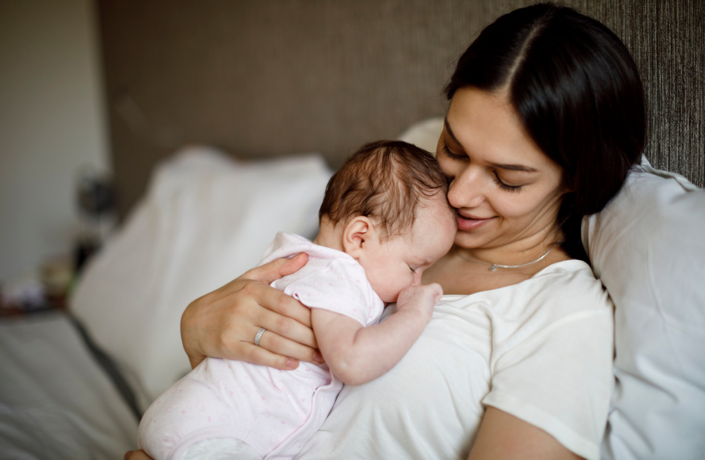 Junge Mutter stitz im Bett und hält ihr Baby mit türkischem Mädchennamen im Arm