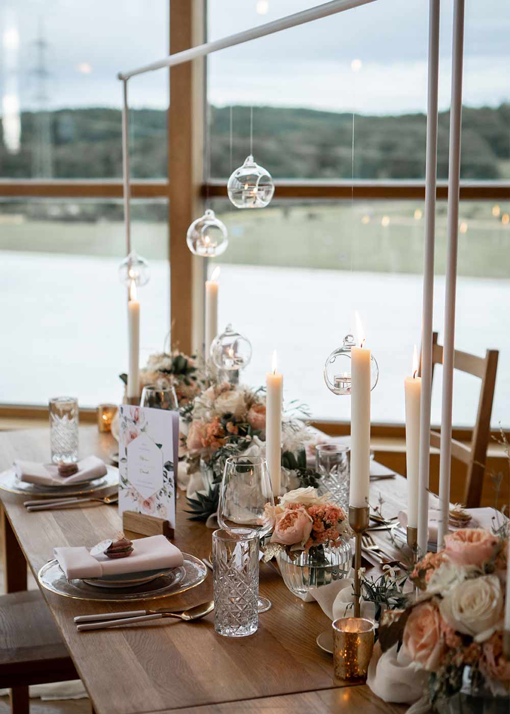 Hochzeitstafel aus Holz dekoriert mit Kerzen in Weiß und sanften Blumen.