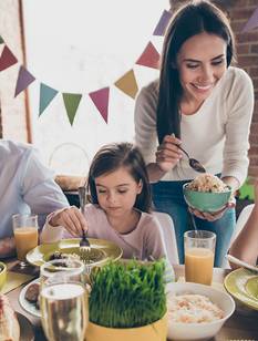 Eine Familie sitzt zum Osterbrunch zusammen. Den Tisch zieren österliche Leckereien.