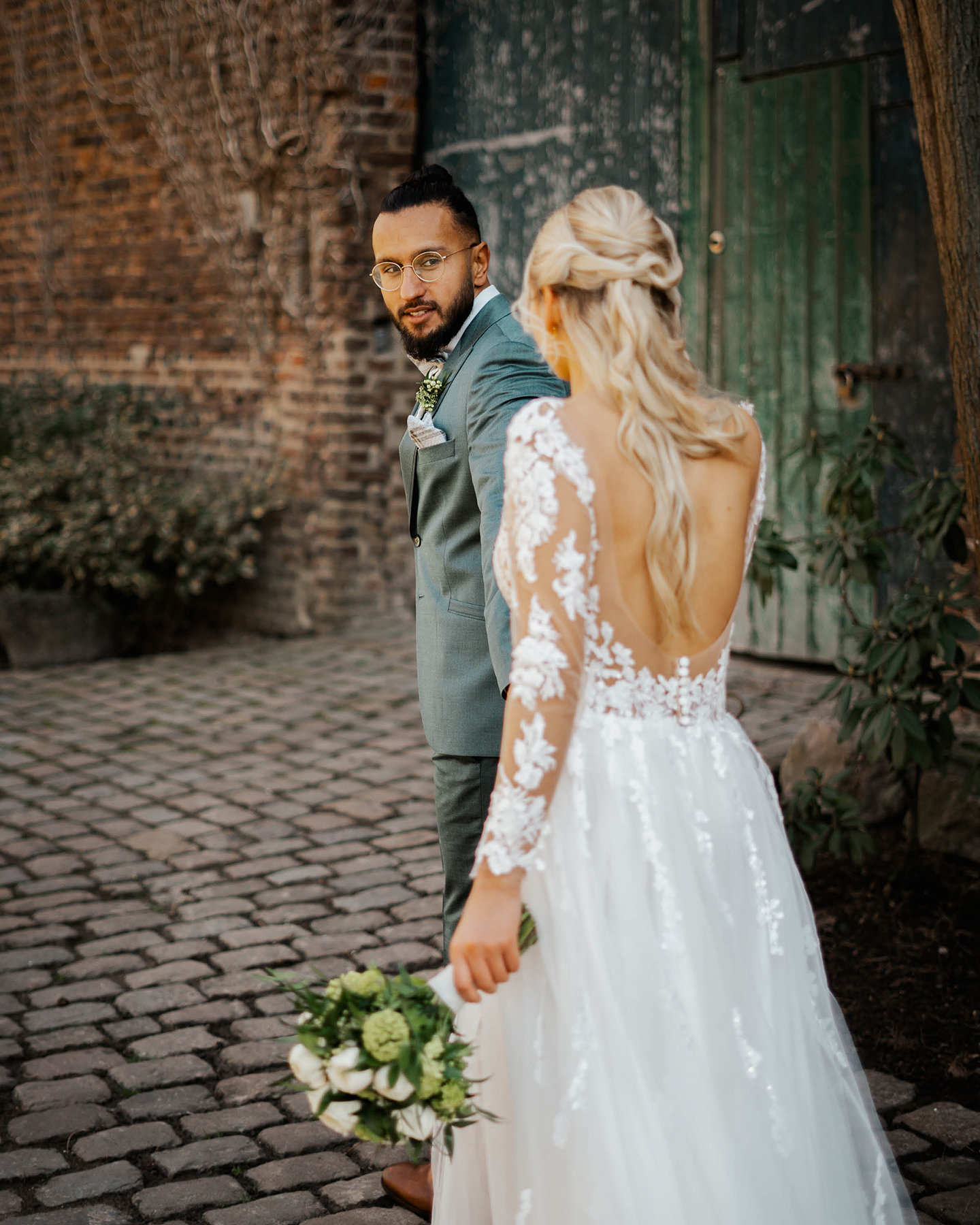  Bräutigam hält Braut an der Hand und schaut sie an. Im Hintergrund ist das Scheunentor der Hochzeitslocation zu sehen.