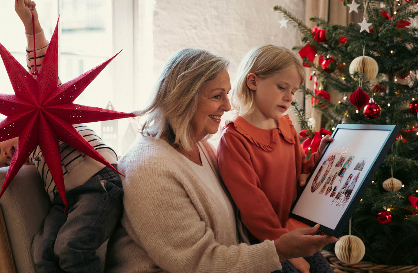 Oma sitzt mit Enkelkindern vor dem Weihnachtsbaum.