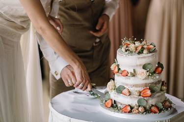 Brautpaar schneidet die drei stöckige Hochzeitstorte an, die mit Blumen und frischen Erdbeeren verziert ist