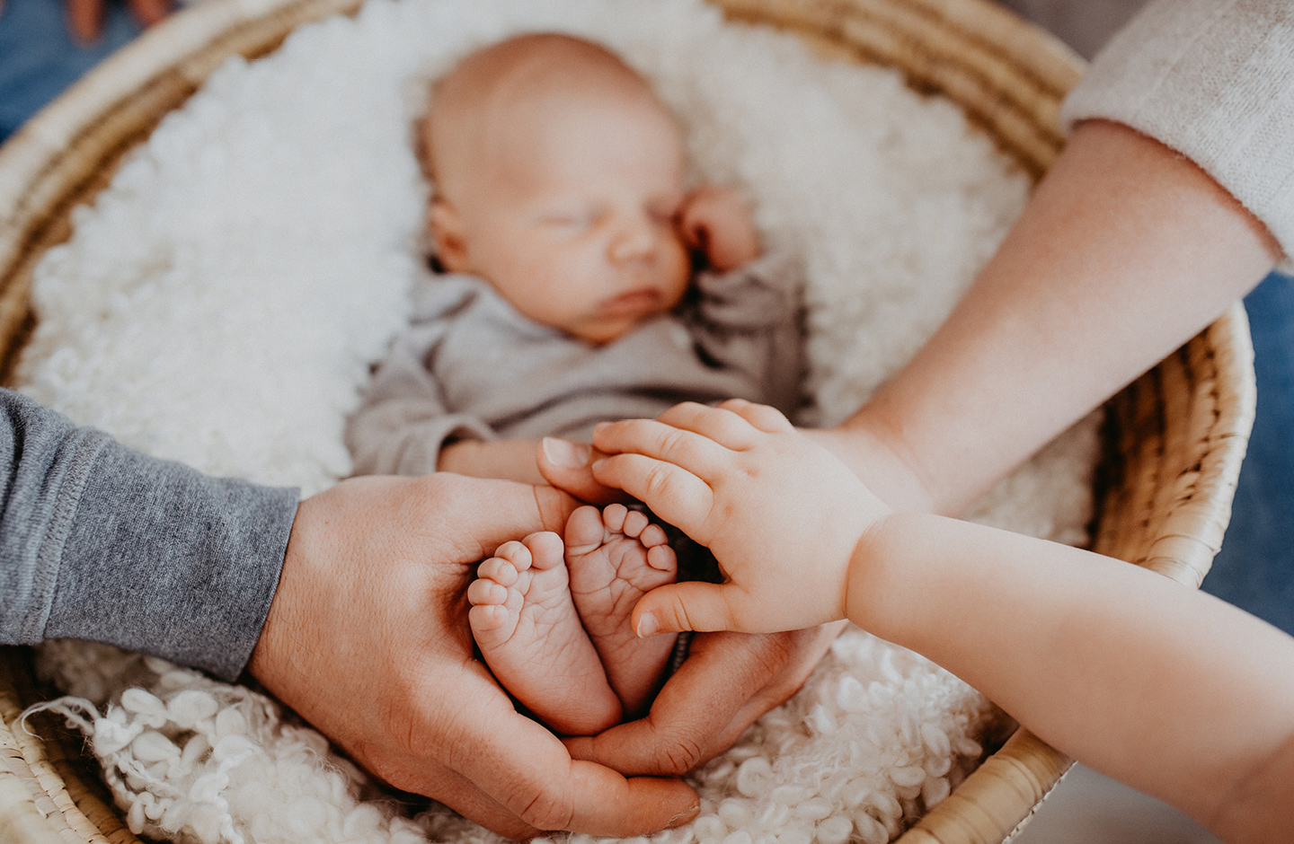 Mama, Papa und Schwester halten Hände um die Füße des Neugeborenen mit einem nordischen Mädchennamen.